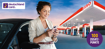 Eine Person am Telefon, die vor einem Auto an einer Esso-Tankstelle steht